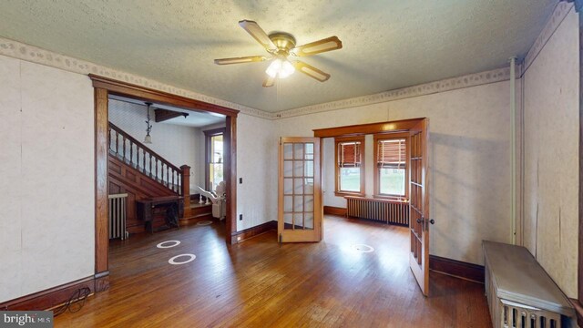 unfurnished room with french doors, a textured ceiling, wood finished floors, stairway, and radiator