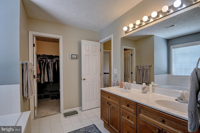 bathroom featuring vanity, a textured ceiling, tile patterned flooring, and a bath