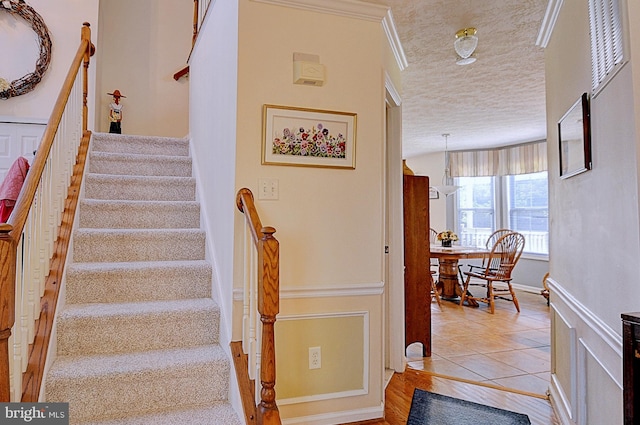 stairway featuring a textured ceiling, tile patterned flooring, and ornamental molding