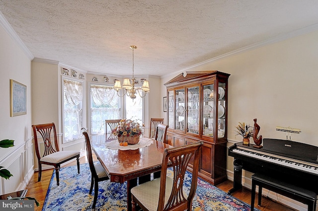 dining room featuring an inviting chandelier, wood-type flooring, a textured ceiling, and ornamental molding