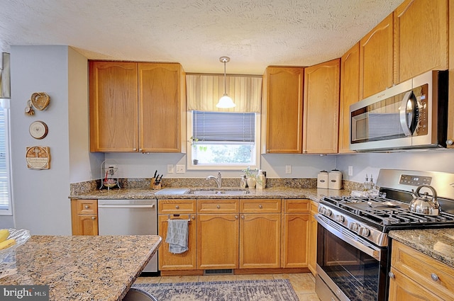 kitchen with appliances with stainless steel finishes, light stone countertops, a textured ceiling, decorative light fixtures, and sink