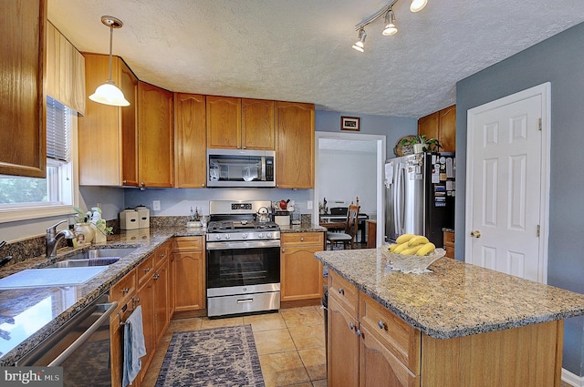 kitchen featuring light stone counters, hanging light fixtures, a textured ceiling, stainless steel appliances, and a center island