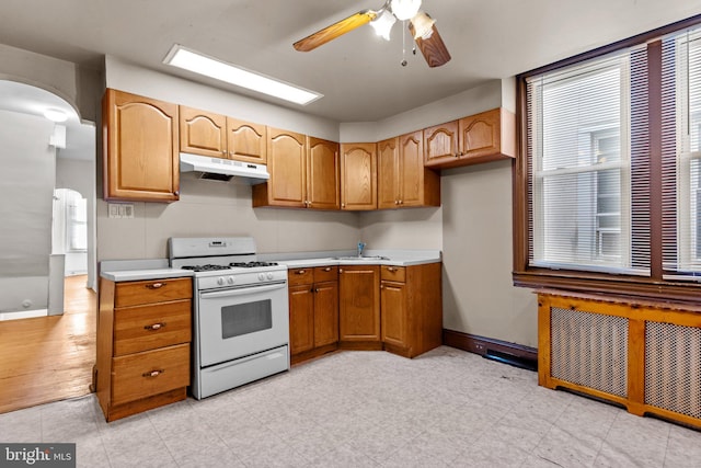 kitchen featuring white gas range, ceiling fan, sink, light hardwood / wood-style floors, and radiator