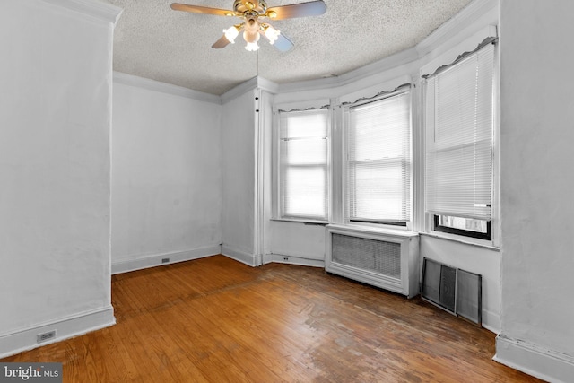 empty room with ceiling fan, hardwood / wood-style flooring, ornamental molding, radiator, and a textured ceiling