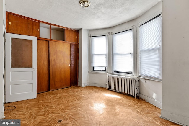 unfurnished bedroom with a textured ceiling, a closet, radiator heating unit, and light parquet floors