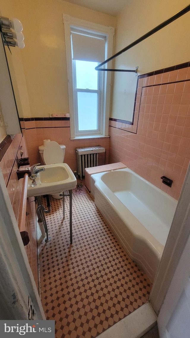 bathroom featuring tiled shower / bath, tile walls, toilet, and radiator heating unit