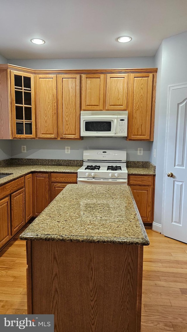 kitchen featuring white appliances, a kitchen island, light stone countertops, light wood-type flooring, and sink