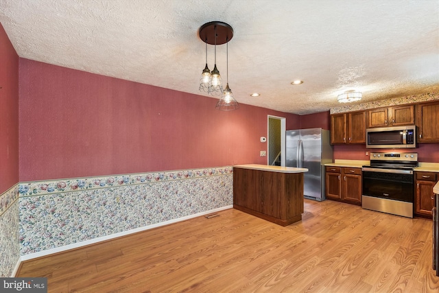 kitchen featuring kitchen peninsula, stainless steel appliances, decorative light fixtures, light wood-type flooring, and a textured ceiling