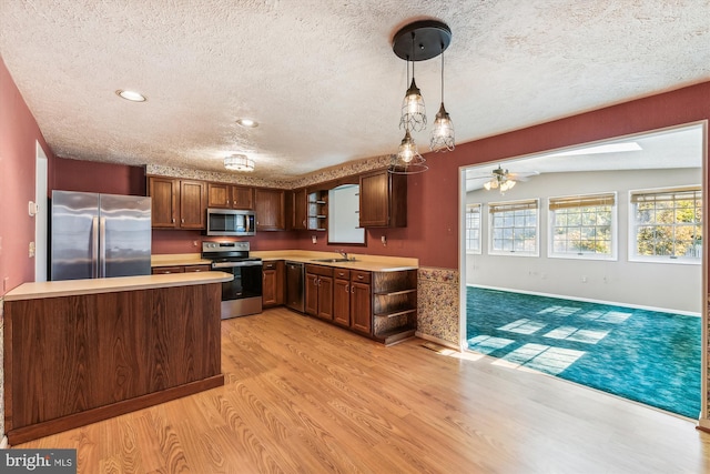 kitchen with hanging light fixtures, sink, lofted ceiling with skylight, appliances with stainless steel finishes, and light hardwood / wood-style floors