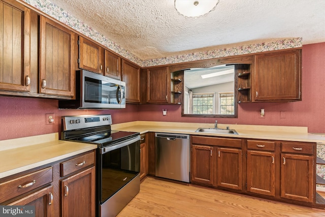 kitchen with light hardwood / wood-style floors, a textured ceiling, appliances with stainless steel finishes, and sink