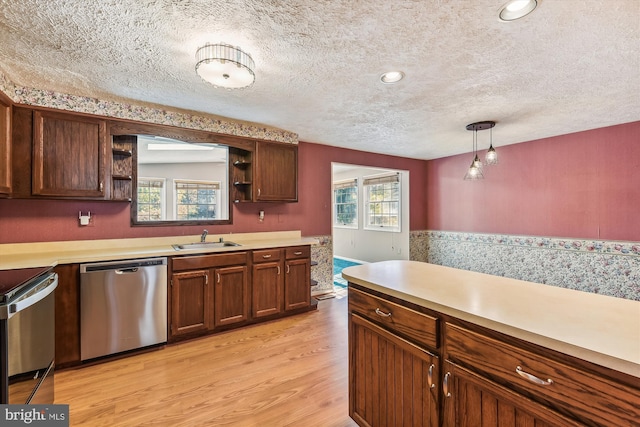 kitchen with hanging light fixtures, appliances with stainless steel finishes, a textured ceiling, light wood-type flooring, and sink