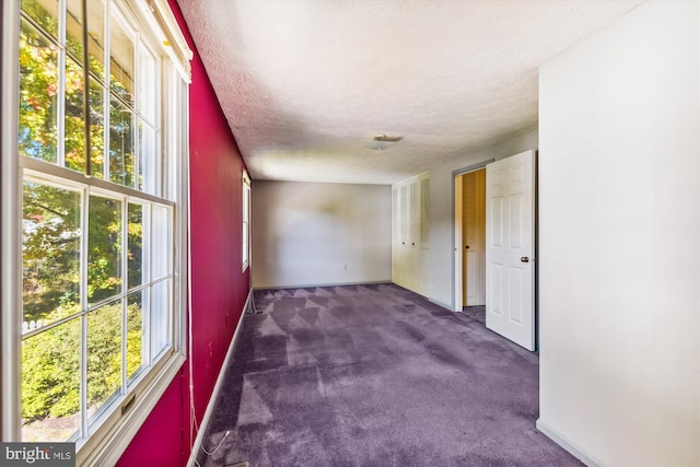 spare room featuring a textured ceiling, a wealth of natural light, and dark colored carpet