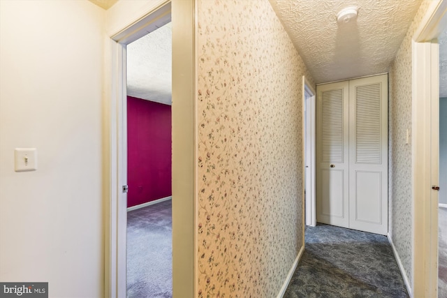 hall with a textured ceiling and dark carpet