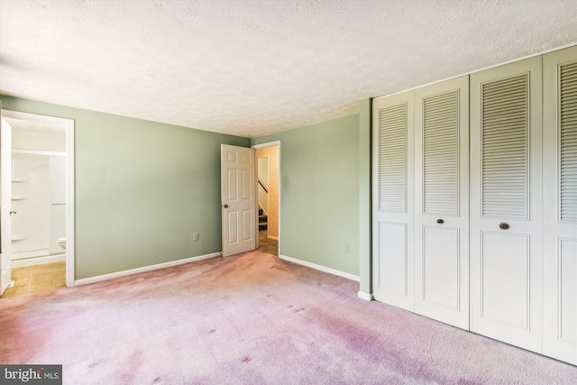 unfurnished bedroom with a textured ceiling, ensuite bathroom, and light colored carpet