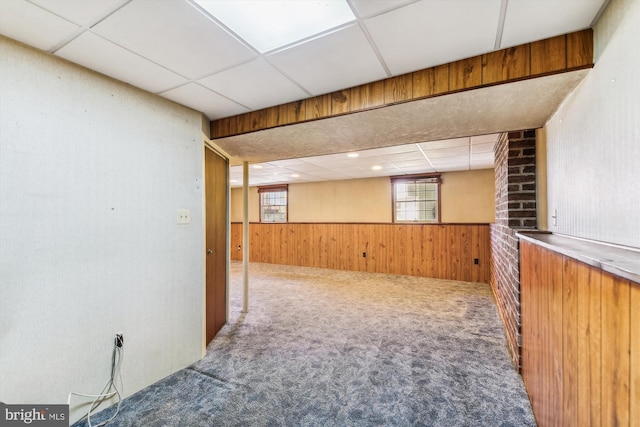 interior space with wood walls, a drop ceiling, and carpet floors