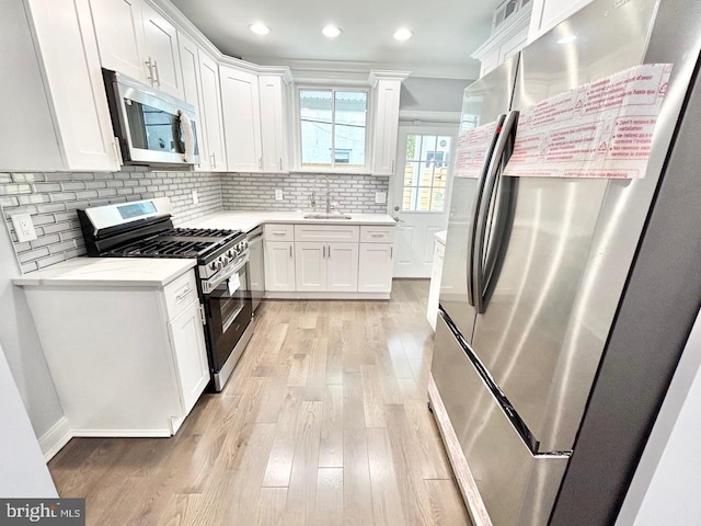 kitchen with stainless steel appliances, backsplash, sink, white cabinets, and light hardwood / wood-style flooring