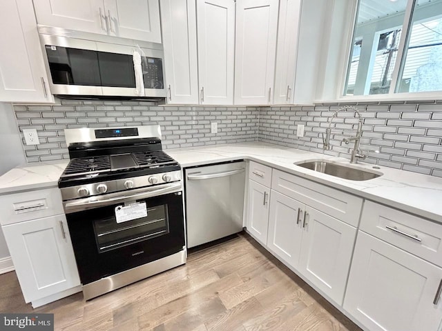 kitchen with white cabinetry, sink, light stone counters, appliances with stainless steel finishes, and light hardwood / wood-style flooring