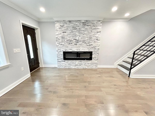 unfurnished living room with a stone fireplace, wood-type flooring, and crown molding