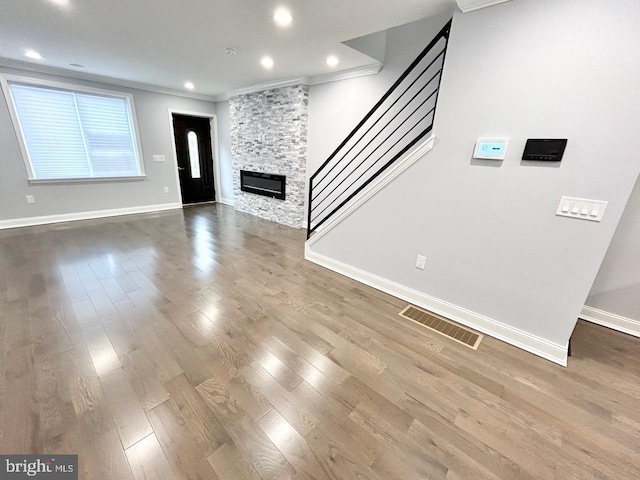 unfurnished living room featuring a stone fireplace, wood-type flooring, and crown molding