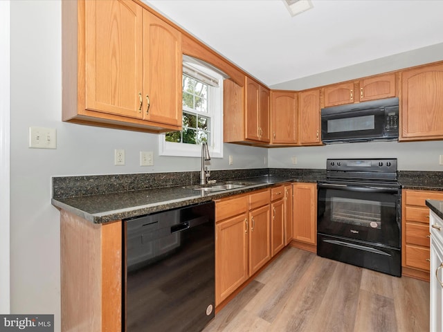 kitchen featuring dark stone counters, black appliances, sink, and light wood-type flooring