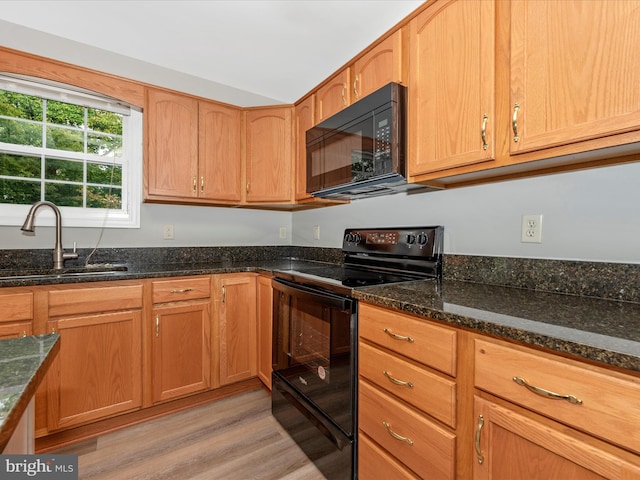 kitchen with dark stone countertops, light hardwood / wood-style flooring, sink, and black appliances