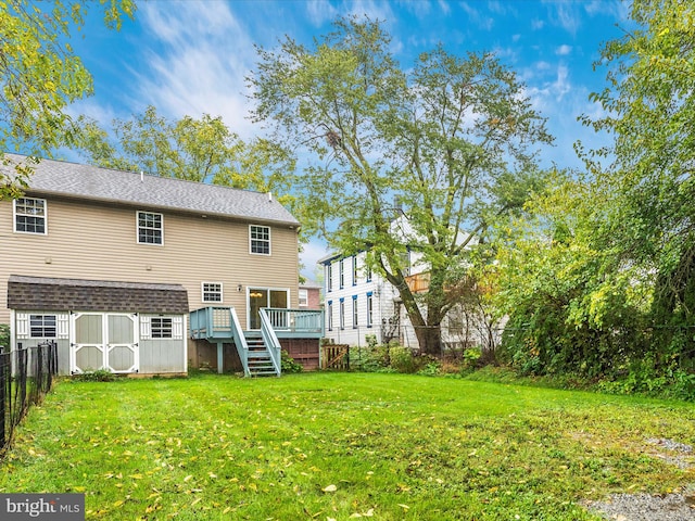 rear view of house featuring a wooden deck, a lawn, and a storage unit