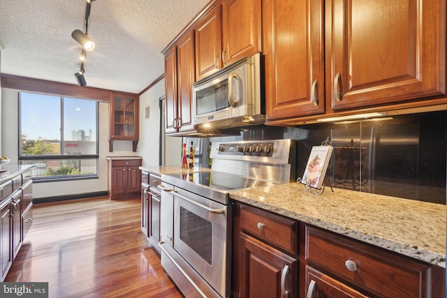 kitchen featuring light stone counters, a textured ceiling, rail lighting, stainless steel appliances, and light hardwood / wood-style floors