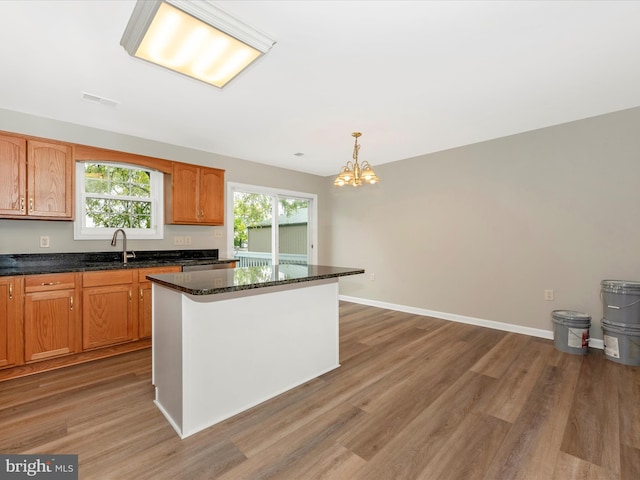 kitchen featuring a kitchen island, hardwood / wood-style flooring, dark stone countertops, hanging light fixtures, and an inviting chandelier