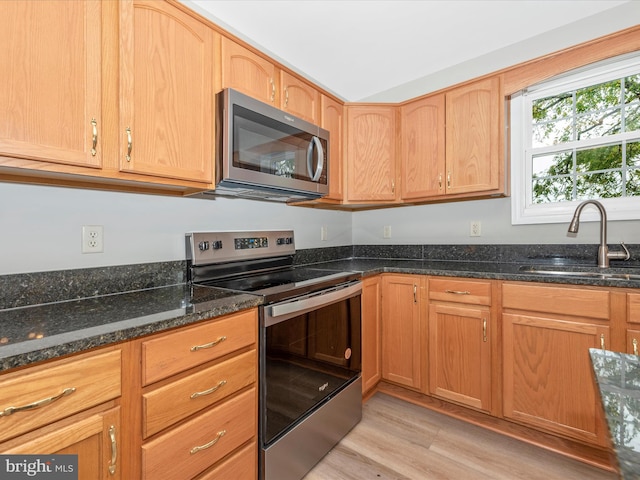 kitchen featuring dark stone countertops, sink, stainless steel appliances, and light hardwood / wood-style flooring