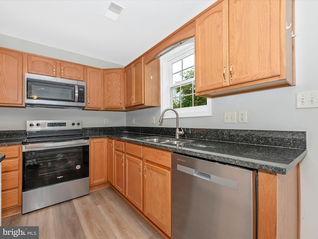 kitchen with sink, stainless steel appliances, light hardwood / wood-style floors, and dark stone counters