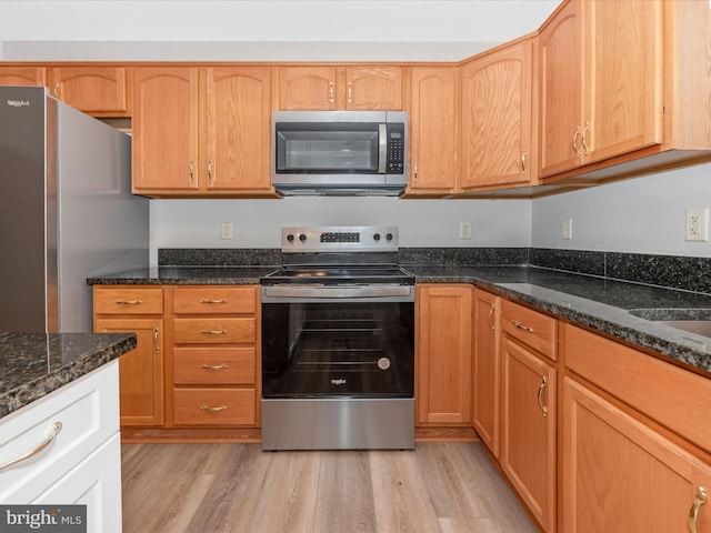 kitchen with stainless steel appliances, dark stone countertops, and light wood-type flooring