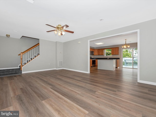 unfurnished living room with ceiling fan with notable chandelier, dark wood-type flooring, and sink