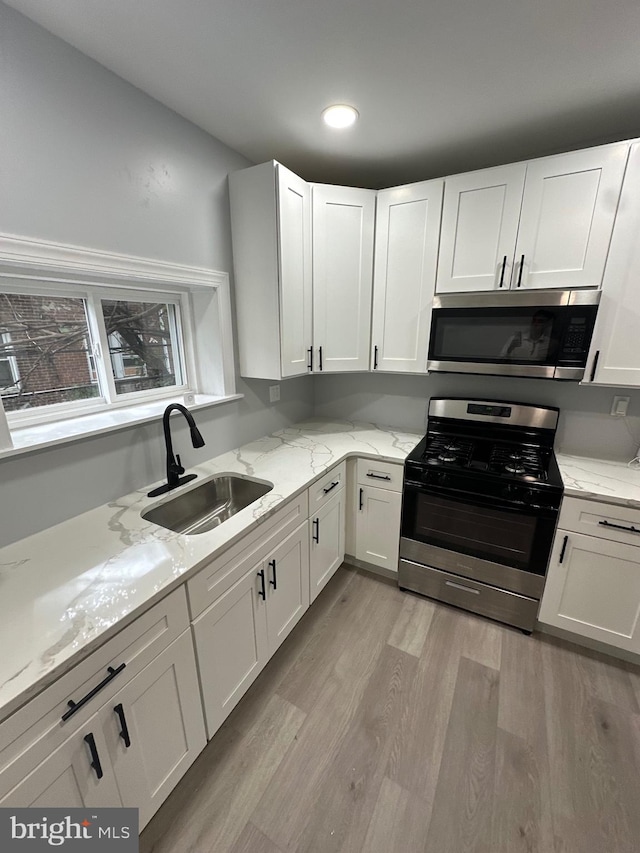 kitchen featuring light wood-type flooring, sink, white cabinets, appliances with stainless steel finishes, and light stone countertops