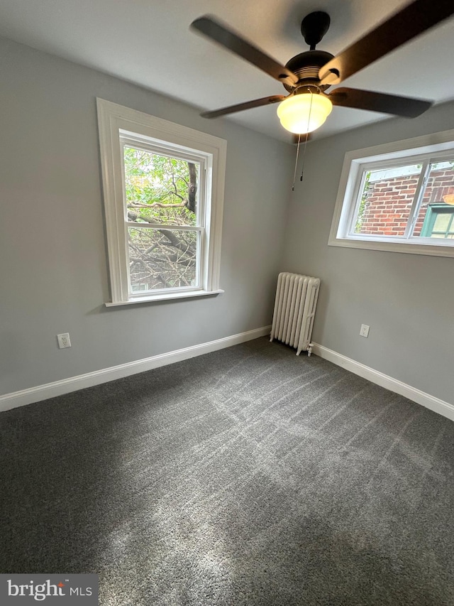 empty room featuring ceiling fan, radiator, carpet flooring, and a wealth of natural light