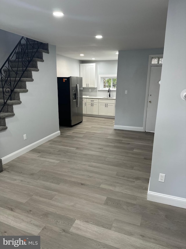 kitchen featuring light wood-type flooring, stainless steel refrigerator with ice dispenser, white cabinetry, and sink