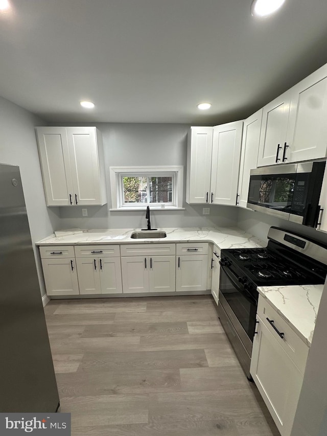 kitchen with stainless steel appliances, white cabinets, light stone counters, and sink