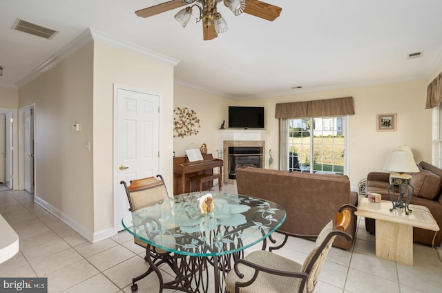 tiled dining room featuring ceiling fan, crown molding, and a tiled fireplace