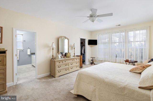 bedroom featuring connected bathroom, a closet, ceiling fan, a walk in closet, and light colored carpet