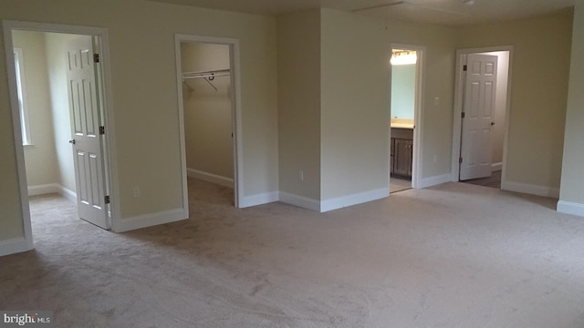 unfurnished bedroom with ensuite bath, light carpet, a walk in closet, and a closet