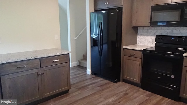 kitchen with light stone counters, dark brown cabinets, black appliances, dark hardwood / wood-style flooring, and decorative backsplash