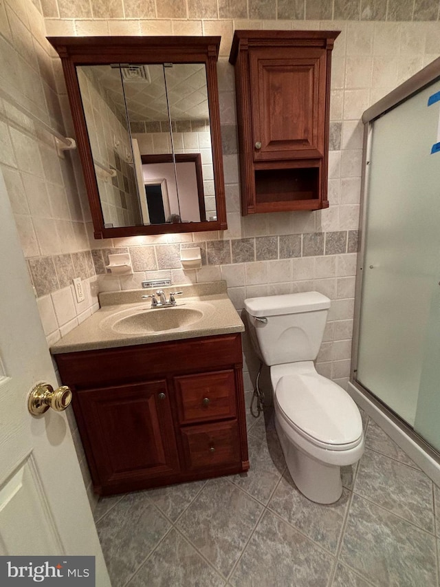 bathroom with tile walls, vanity, toilet, and a shower with shower door