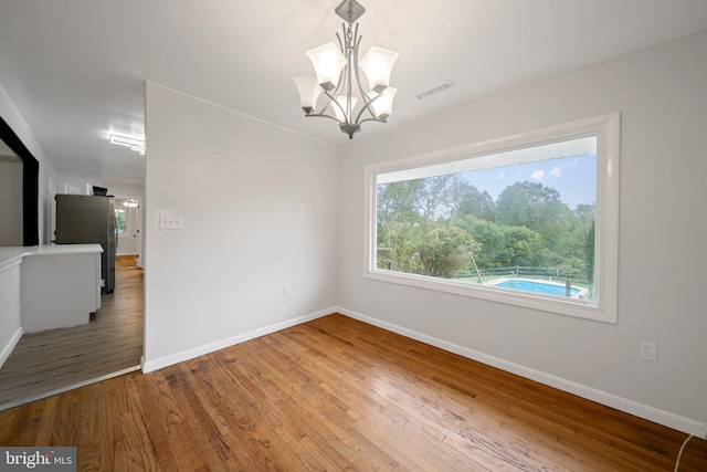 spare room with wood-type flooring and an inviting chandelier