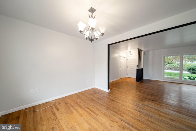 empty room with wood-type flooring and a notable chandelier