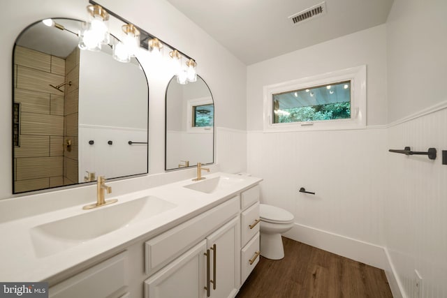 bathroom with a tile shower, vanity, hardwood / wood-style floors, and toilet