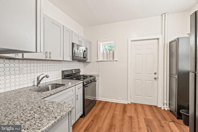 kitchen featuring light stone counters, light hardwood / wood-style floors, sink, backsplash, and appliances with stainless steel finishes