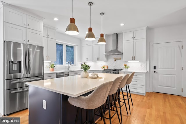 kitchen featuring white cabinets, wall chimney exhaust hood, light hardwood / wood-style flooring, decorative light fixtures, and appliances with stainless steel finishes