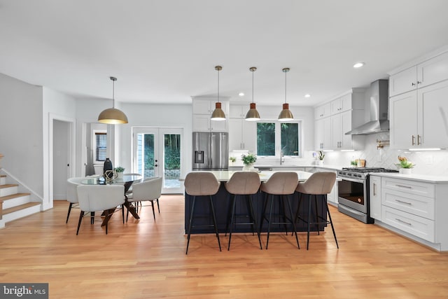 kitchen featuring wall chimney exhaust hood, stainless steel appliances, white cabinetry, and pendant lighting