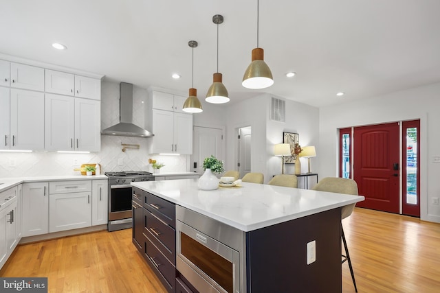 kitchen featuring white cabinets, wall chimney range hood, stainless steel appliances, a center island, and a breakfast bar area