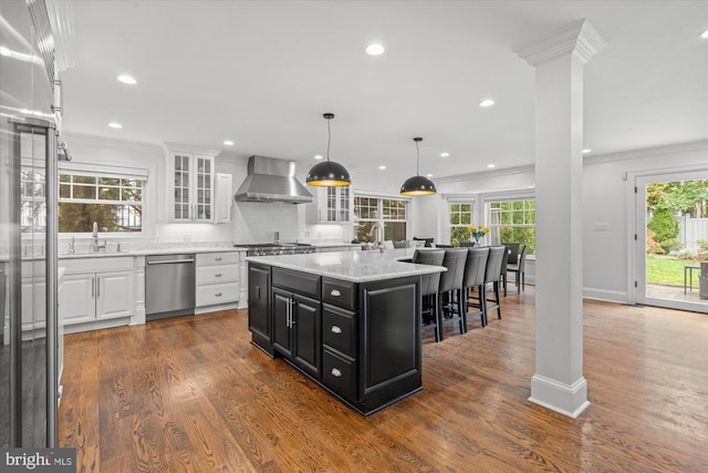 kitchen with a kitchen island, wood-type flooring, stainless steel appliances, white cabinets, and wall chimney exhaust hood