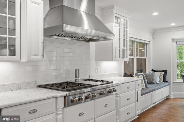 kitchen with tasteful backsplash, wall chimney range hood, ornamental molding, and white cabinets